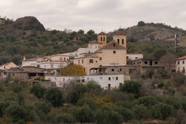 pieni kaupunki vuoren puolella Etelä-Espanjassa, on kirkko, sen talot ovat valkoisia maalattuja julkisivuja, on puita ja pensaita, taivaalla on pilvi - Valokuva, kuva
