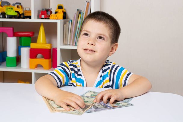 Un bel bambino e banconote da un dollaro. Il ragazzo sta pensando a dove spendere i soldi. alfabetizzazione finanziaria per i bambini - Foto, immagini