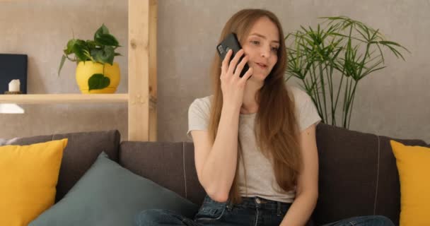 Mujer joven hablando por teléfono y sonriendo. Chica hablar por teléfono en casa en la sala de estar - Metraje, vídeo