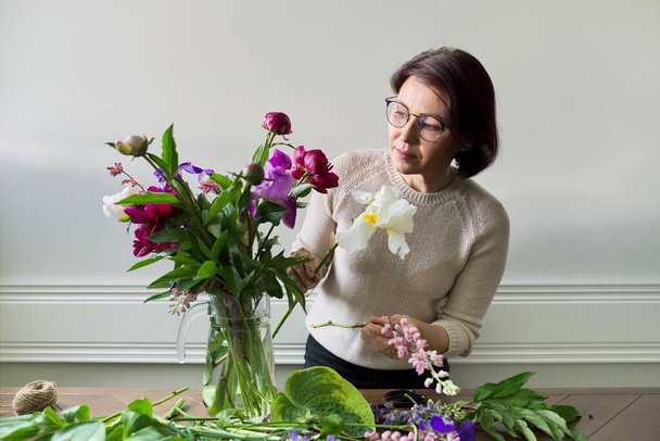 Mature woman at home with spring flowers - Fotoğraf, Görsel