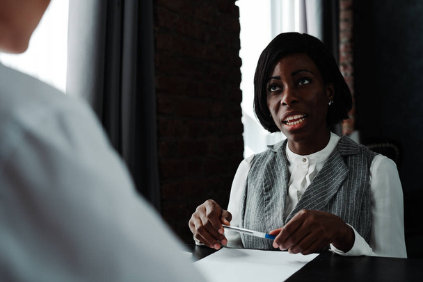 Serious african american woman sitting at a table and having a job interview holding a pen - Фото, зображення