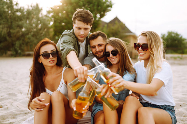The young friends holding bottles with beer at the beach party. Group of friends having fun, relaxing, toasting with beerus. People, lifestyle, travel, nature and vacations concept. - Photo, image