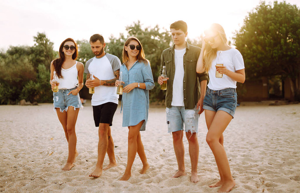 The young friends holding bottles with beer at the beach party. Group of friends having fun, relaxing, toasting with beerus. People, lifestyle, travel, nature and vacations concept. - Foto, Bild