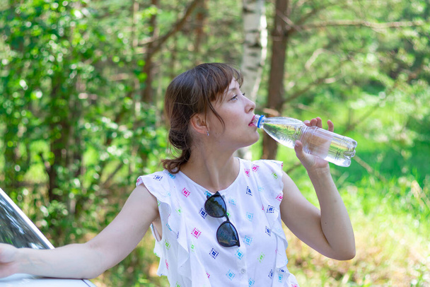 Krásná mladá žena pije vodu za letního slunečného dne na pozadí zeleného listí. Selektivní zaměření - Fotografie, Obrázek