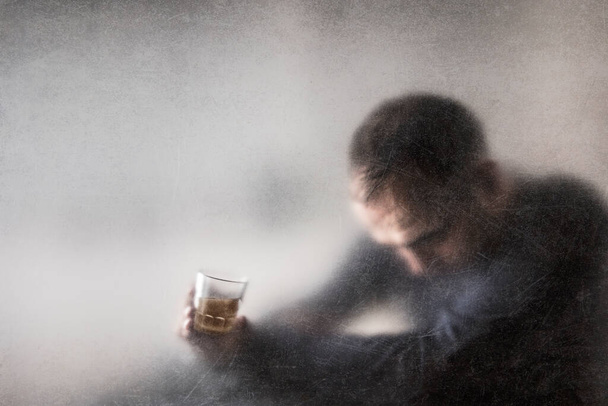 Un hombre con un vaso de whisky detrás de un polvoriento vaso rayado. Concepto de alcoholismo. - Foto, Imagen