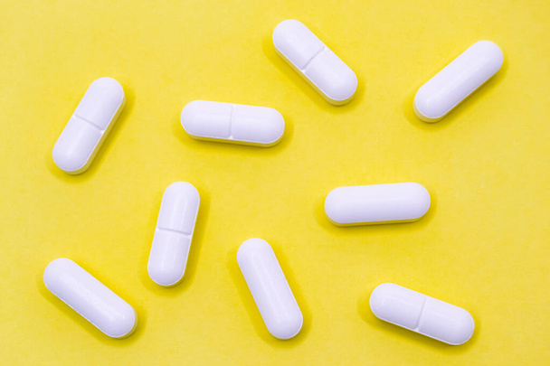 Set of white pills on a yellow background. Horizontal photography. - Foto, afbeelding