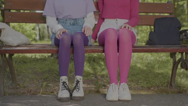Mallas brillantes en las piernas de las adolescentes sentadas en un banco del parque. Detalles en el estilo de la ropa. - Metraje, vídeo