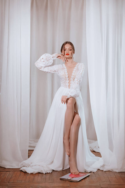 Hermosa novia morena con maquillaje ligero en vestido blanco en un exquisito interior  - Foto, Imagen