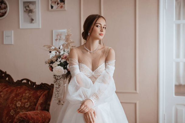 Hermosa novia con maquillaje ligero en vestido blanco en un exquisito interior  - Foto, imagen