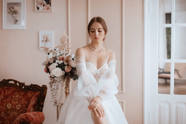 Hermosa novia con maquillaje ligero en vestido blanco en un exquisito interior  - Foto, imagen