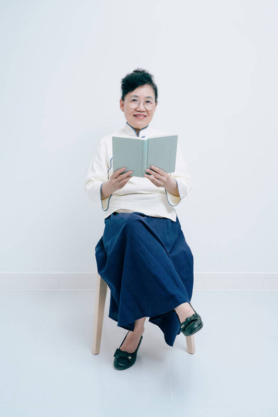 Middelbare leeftijd vrouw draagt traditionele Chinese kostuum is het lezen - Foto, afbeelding