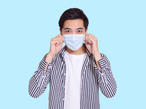 De knappe jongeman draagt een beschermend medisch masker om COVID-19 infectie te voorkomen en raakt het masker aan voor inspectie. - Foto, afbeelding