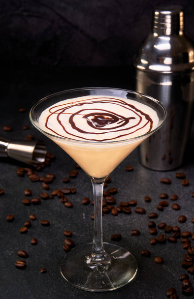 Crema irlandesa y cóctel de café en un vaso con un remolino de chocolate en la parte superior sobre una superficie de mármol negro y granos de café. fondo negro con espacio de copia para publicidad. - Foto, Imagen