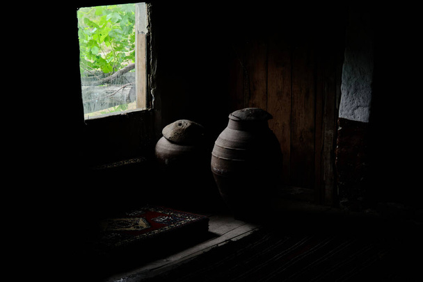 all'interno della vecchia casa di villaggio abbandonata fatta di materiale di legno e ci sono vasi di terracotta di grandi dimensioni vicino alla finestra e erba verde fuori dallo sfondo della finestra. - Foto, immagini