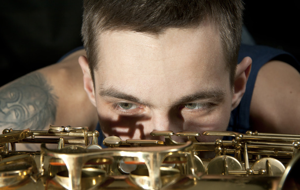 Крупным планом молодой джазовый человек смотрит на саксофон
 - Фото, изображение