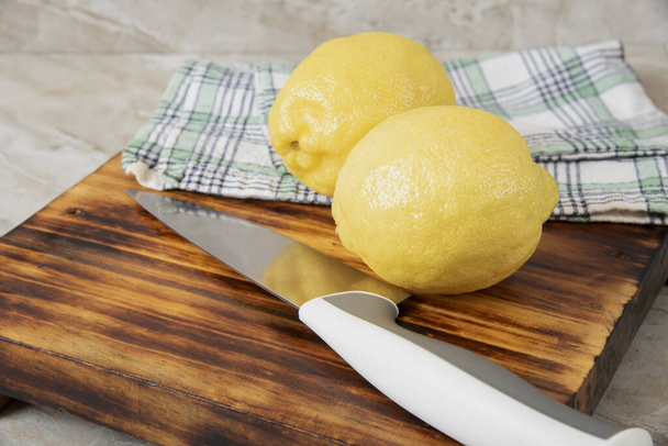 Two fresh lemons on a cutting board with a kitchen knife - Photo, image