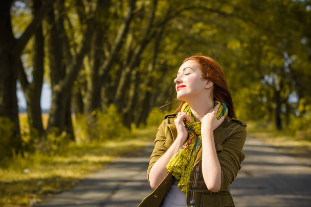 Молодая милая рыжая женщина стильно одета в пиджак, шарф, одежду в зеленых и красных тонах. Леди гуляет по осенней роще деревьев - Фото, изображение