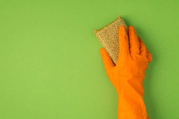 Powyższe zdjęcie gąbki celulozowej i pomarańczowych rękawiczek odizolowanych na zielonym tle - Zdjęcie, obraz