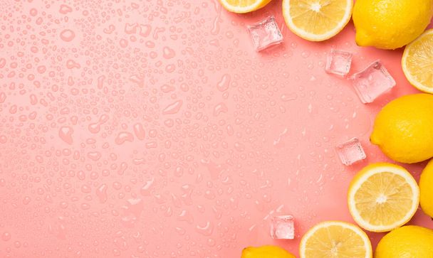 Вид сверху фото половинки и целые желтые сочные лимоны кубики льда капли на изолированном пастельно-розовом фоне с копирайтом слева - Фото, изображение