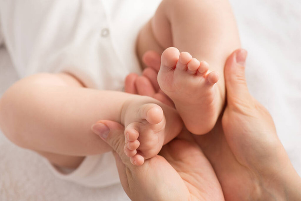 Zbliżenie zdjęcie dłoni matki trzymającej maleńkie nóżki noworodka na białym tle włókienniczym - Zdjęcie, obraz