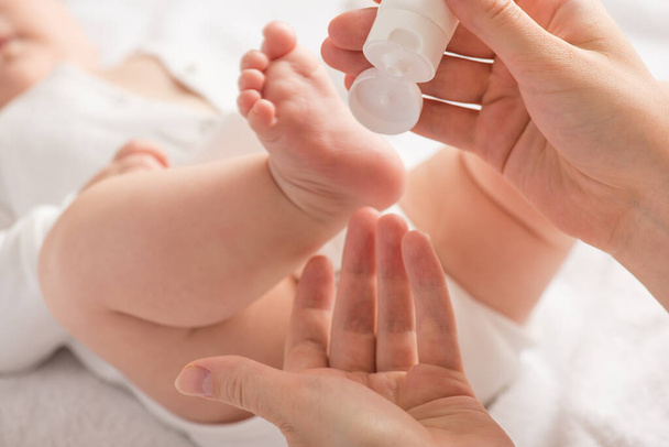 Zbliżenie zdjęcie nóg noworodka i rąk matki trzymających białą kremową rurkę na białym tle - Zdjęcie, obraz