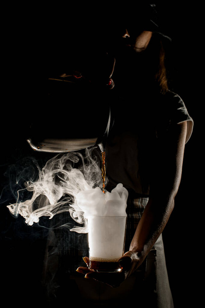 woman in the dark holds steaming cup and pouring drink into it - Foto, Imagem