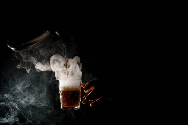 Female hands at dark pour hot coffee from coffee pot into transparent steaming cup - Photo, Image
