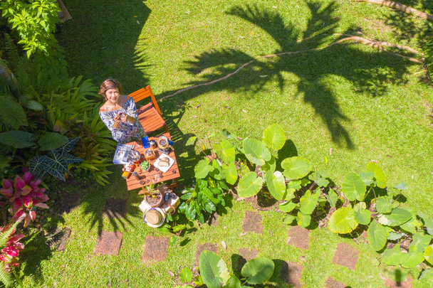 Een vrouw met een glas hete koffie in de groene tuin. Een vrouw ontspannen in de groene tuin met koffie gezet op houten tafel. groene tuin achtergrond. - Foto, afbeelding