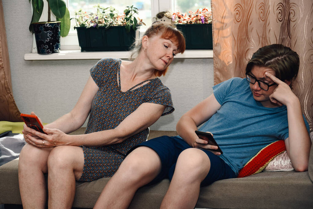 Photo of ordinary family relationships. Mom and teen look at the phone of their son at home while sitting on the sofa - Valokuva, kuva