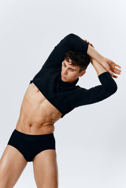 a young man with a pumped-up torso in shorts and a sweater bent over to the side on a light background - Photo, Image