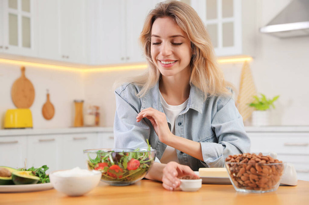 Woman at wooden table with healthy food in kitchen. Keto diet - Foto, afbeelding