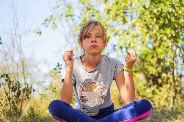 Defocus kaukasischen preteen Mädchen praktiziert Yoga im Park, Wald, im Freien, draußen. Meditation und Konzentration. Wellness gesunder Lebensstil. Porträt eines ernsthaften Mädchens. Grüner Hintergrund. Unscharf. - Foto, Bild