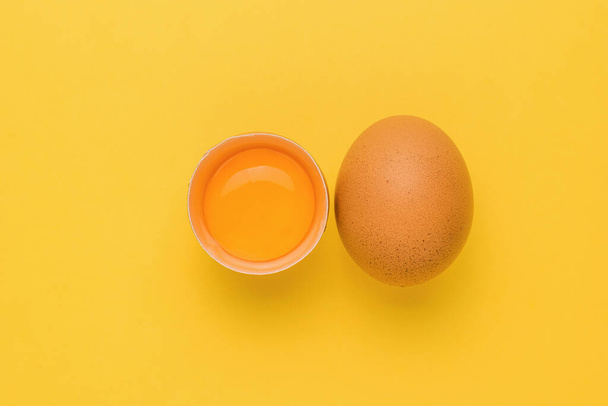 A whole and broken brown chicken egg on a yellow background. A natural product. - Photo, Image