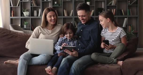 Couple and little children relax on couch using diverse devices - Séquence, vidéo