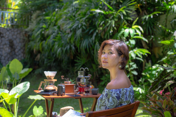Una mujer leyendo una revista en el jardín verde.Una mujer relajarse en el jardín verde con un set de café en la mesa de madera. Fondo de jardín verde. - Foto, imagen