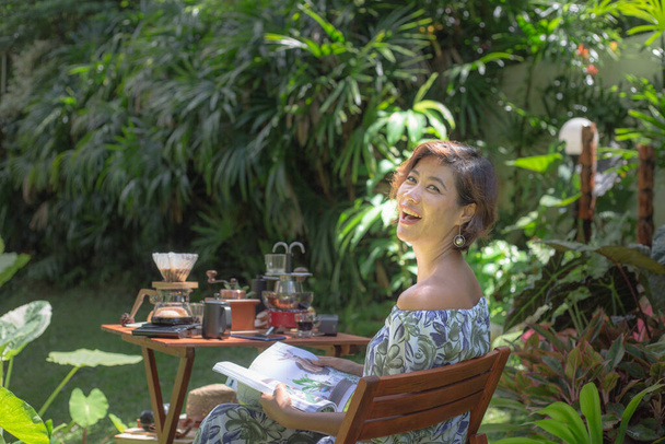 Жінка читає журнал в зеленому саду. Жінка відпочиває в зеленому саду з кавовим набором на дерев'яному столі. зелений фон саду
. - Фото, зображення