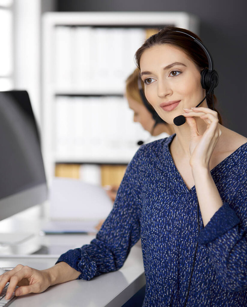 Asian or Latin american businesswoman talking by headset while sitting in office. Call center and diverse people group in business - Фото, изображение