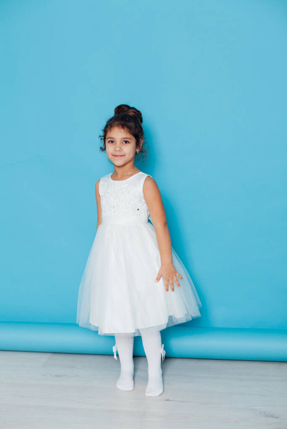 Schöne kleine Mädchen tanzt zu dem Lied in einem weißen Kleid auf blauem Hintergrund - Foto, Bild