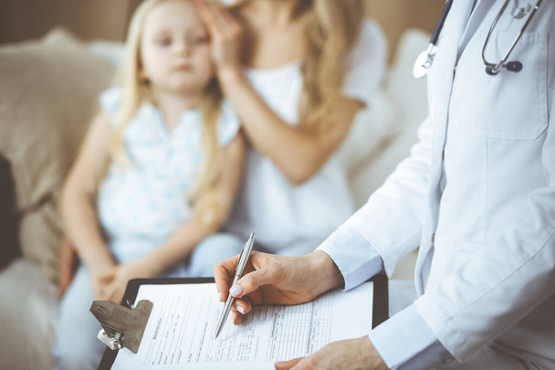Doctor and patient. Pediatrician using clipboard while examining little girl with her mother at home. Sick and unhappy child at medical exam. Medicine concept - Фото, зображення