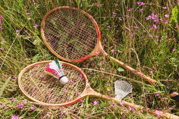 Pair of wooden badminton rackets and two shuttlecocks lie on the meadow grass - Photo, image