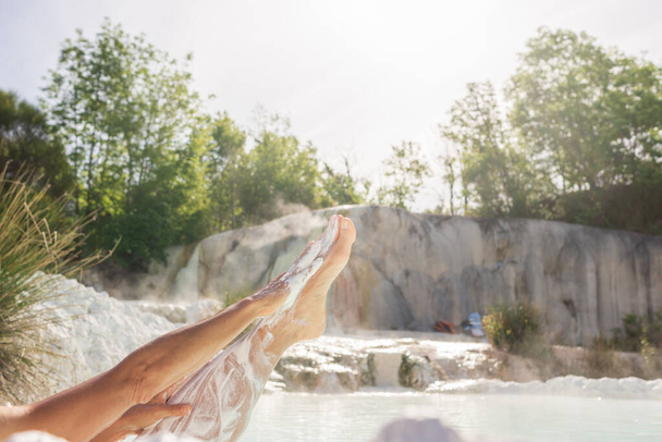 女性の足を閉じて、白い天然泥でスキンケア、地熱プールでの入浴やトスカーナ、イタリアの温泉。Bagniサンフィリッポ熱滝と池、バックライトサンバースト. - 写真・画像