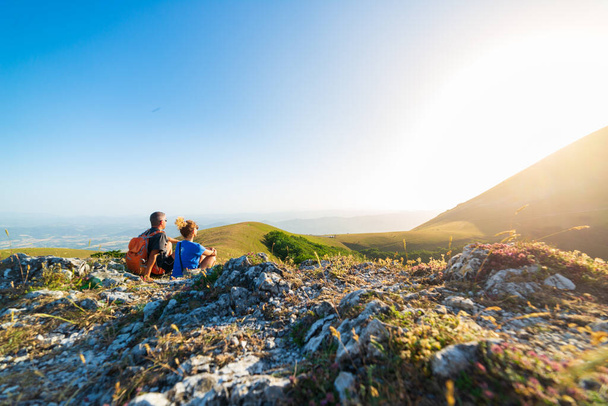Man and woman hiking in the mountains of Umbria region, Monte Cucco, Appennino, Italy. Couple watching sunset together on mountain top. Summer outdoors activity. - Foto, afbeelding