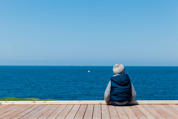 Little boy sits alone and looks at the ships in the sea - Photo, Image
