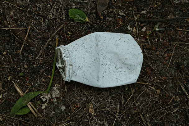 basura de una pequeña botella de plástico blanco yace en el suelo negro afuera - Foto, imagen