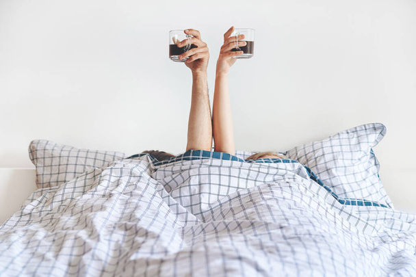 Front view of two hands with cups of coffee at bed  - Fotoğraf, Görsel