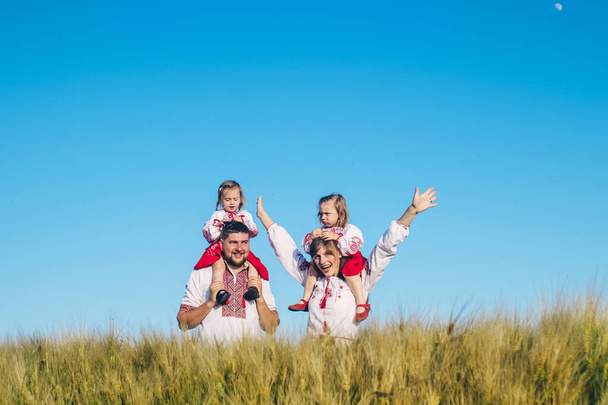 Een familie in een papaverveld gekleed in een nationaal Slavisch kostuum. Mam, pap en tweeling meisjes in geborduurde shirts stoeien op zonnige dag. Concept van een gelukkige jeugd, geschiedenis en saamhorigheid met voorouders - Foto, afbeelding