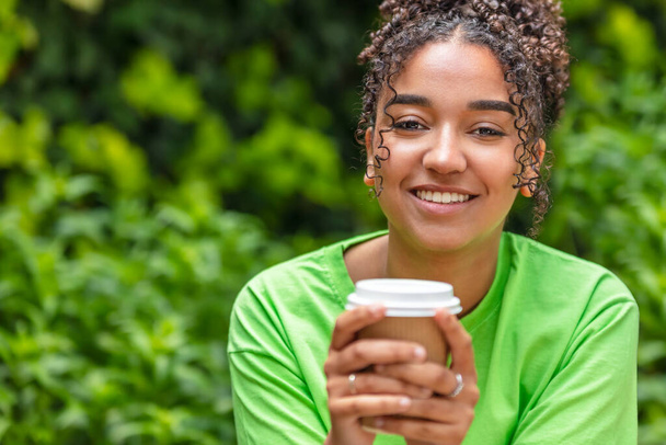 Beautiful happy mixed race African American girl teenager female young woman with perfect teeth smiling drinking takeaway coffee or tea outside  - Fotoğraf, Görsel