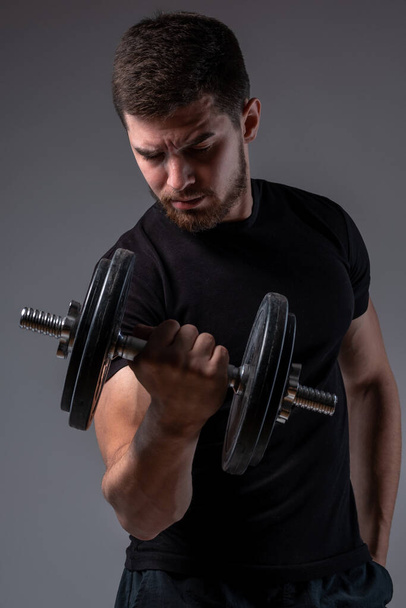 Soustředěný mladý muž provádějící biceps curl s činkou - Fotografie, Obrázek