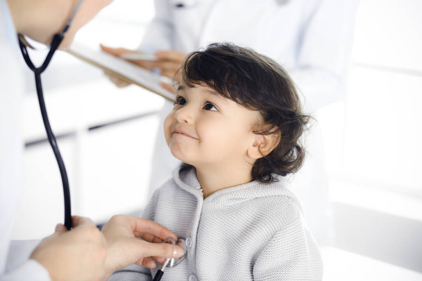 Woman-doctor examining a child patient by stethoscope. Cute arab toddler at physician appointment. Medicine concept - Фото, зображення