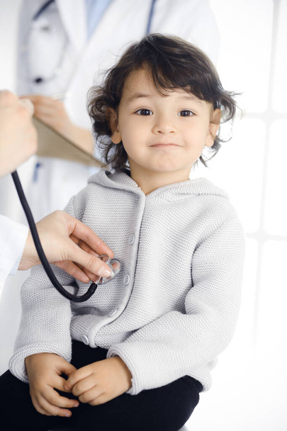 Woman-doctor examining a child patient by stethoscope. Cute arab toddler at physician appointment. Medicine concept - Foto, afbeelding